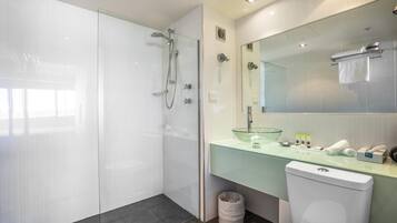 A modern bathroom with a glass shower enclosure, a glass sink, and a toilet.