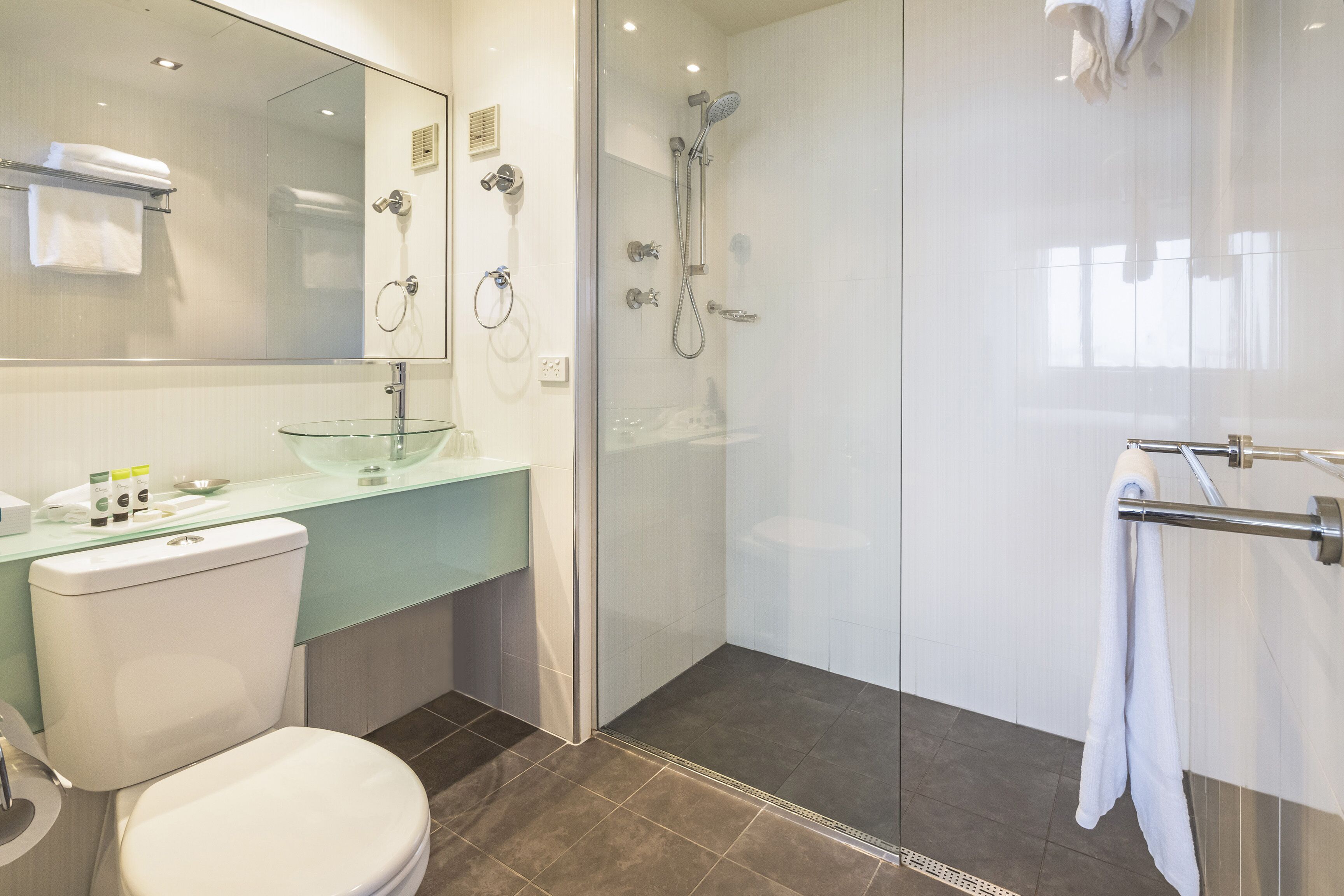 Un baño moderno con cabina de ducha de vidrio, un inodoro blanco y un lavabo de vidrio.