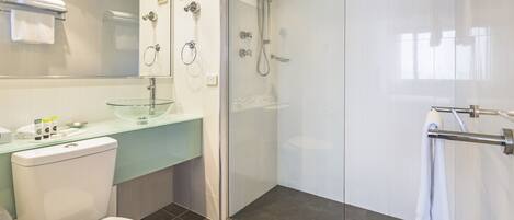 Un baño moderno con cabina de ducha de vidrio, un inodoro blanco y un lavabo de vidrio.
