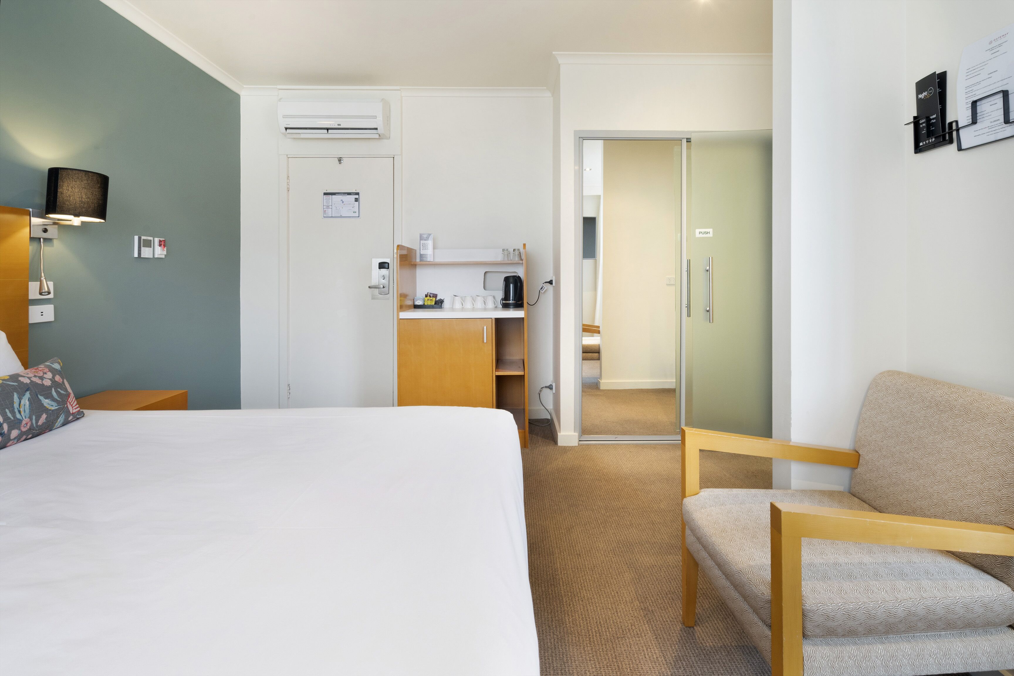 Una habitación de hotel con cama, una silla, escritorio con cafetera y armario.