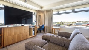 A modern hotel room with a large flat-screen TV, a wooden cabinet, a sofa, and a desk. - Nightelier Devonport Gateway Hotel  (Devonport)
