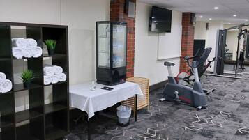 Zona de gimnasio con equipo de ejercicio, dispensador de agua y toallas ordenadas.
