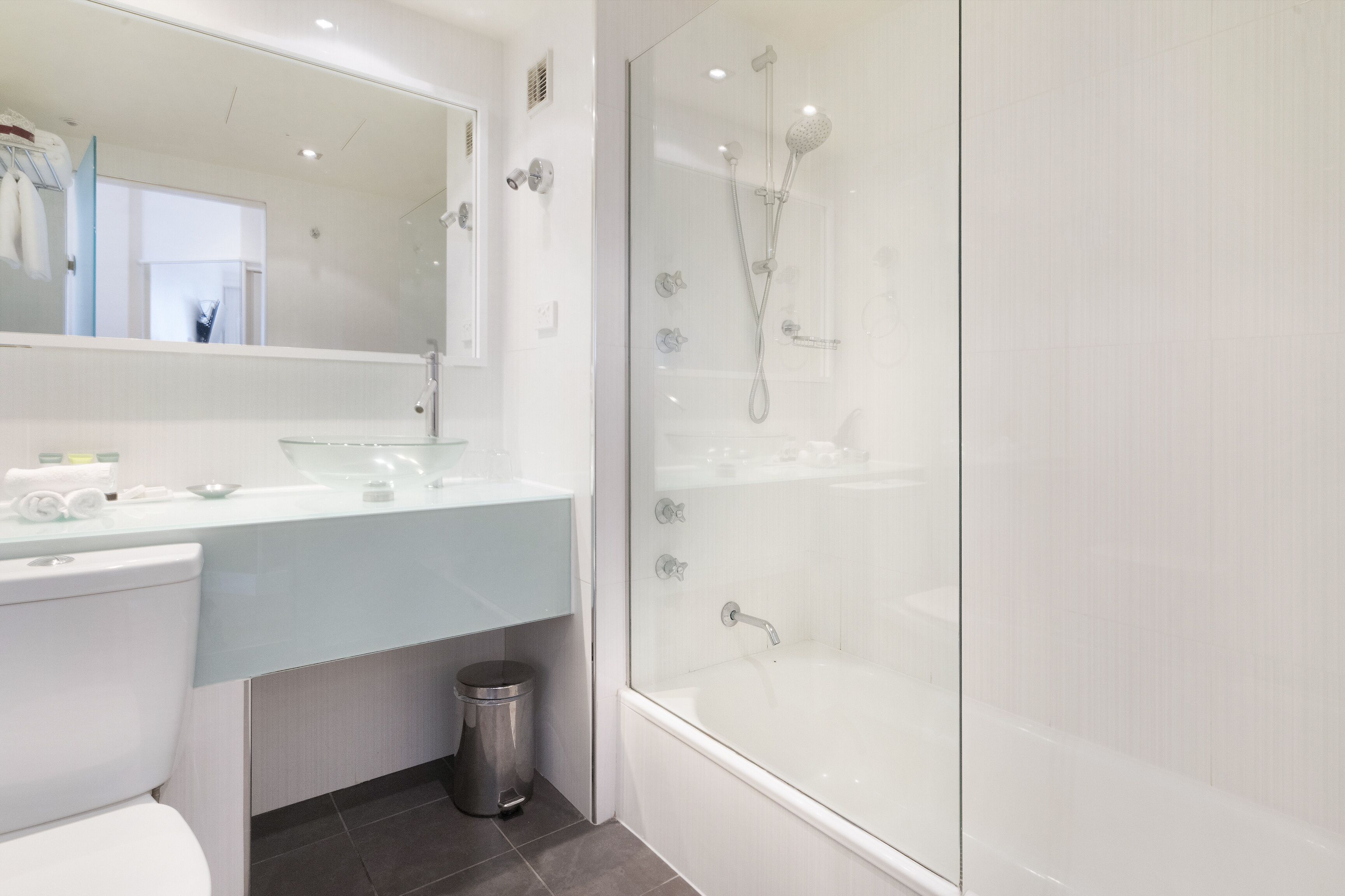 Un baño moderno con ducha de vidrio, lavamanos blanco y retrete.