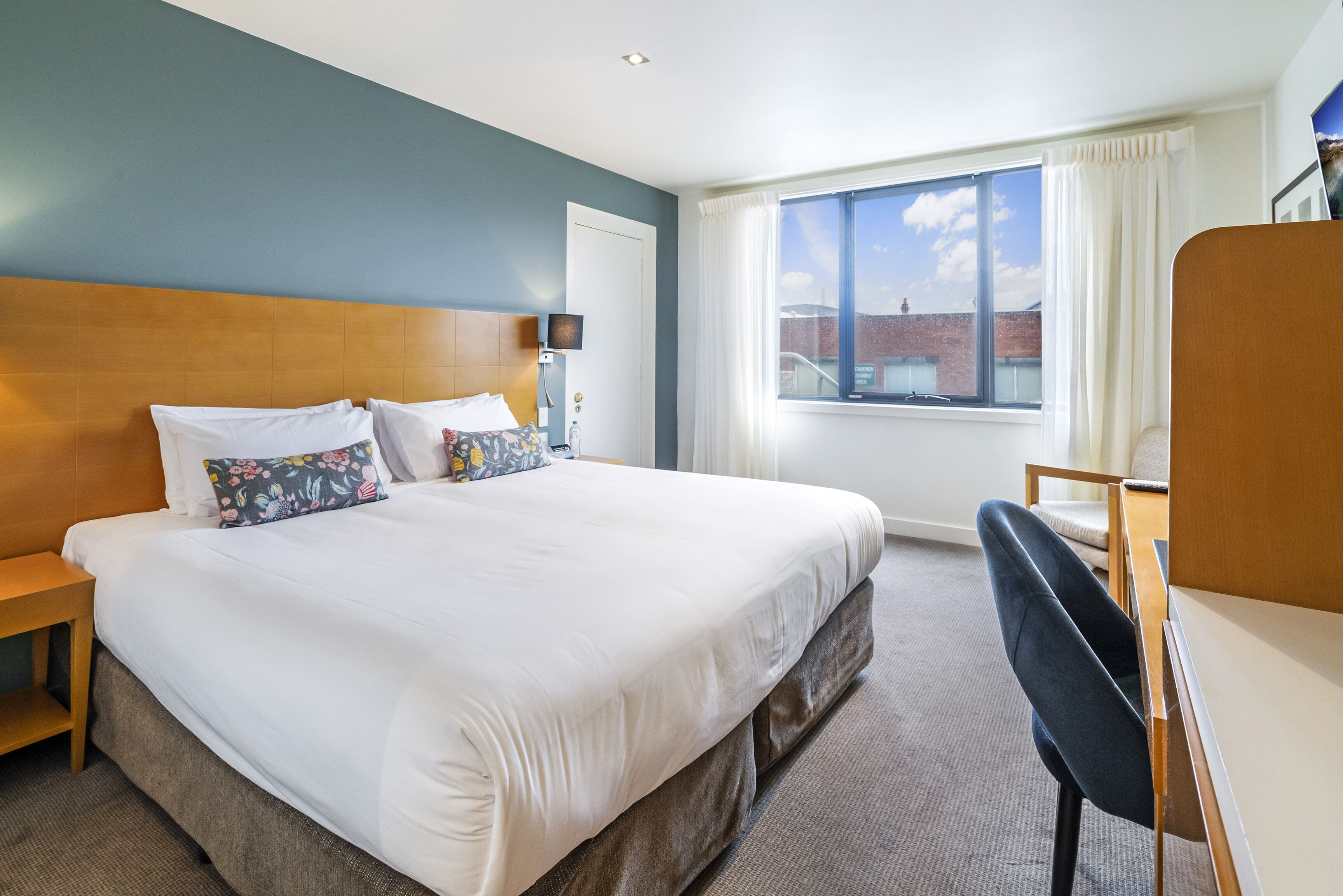 A hotel room with a large bed, a desk, and a window with a view of a building.