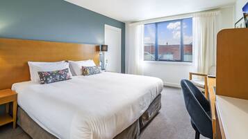 Une chambre d’hôtel avec un grand lit, un bureau et une fenêtre donnant sur un immeuble.