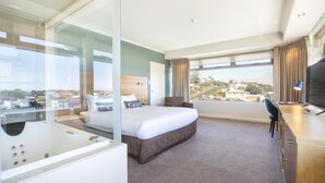 A hotel room with a large bed, a desk, a TV, and a view of the city. - Nightelier Devonport Gateway Hotel  (Devonport)