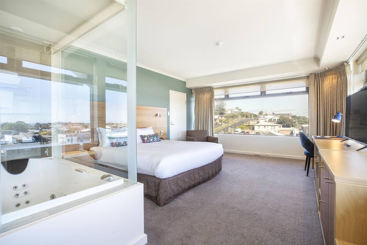 Habitación de hotel con una cama grande, escritorio, televisor y vistas a la ciudad.