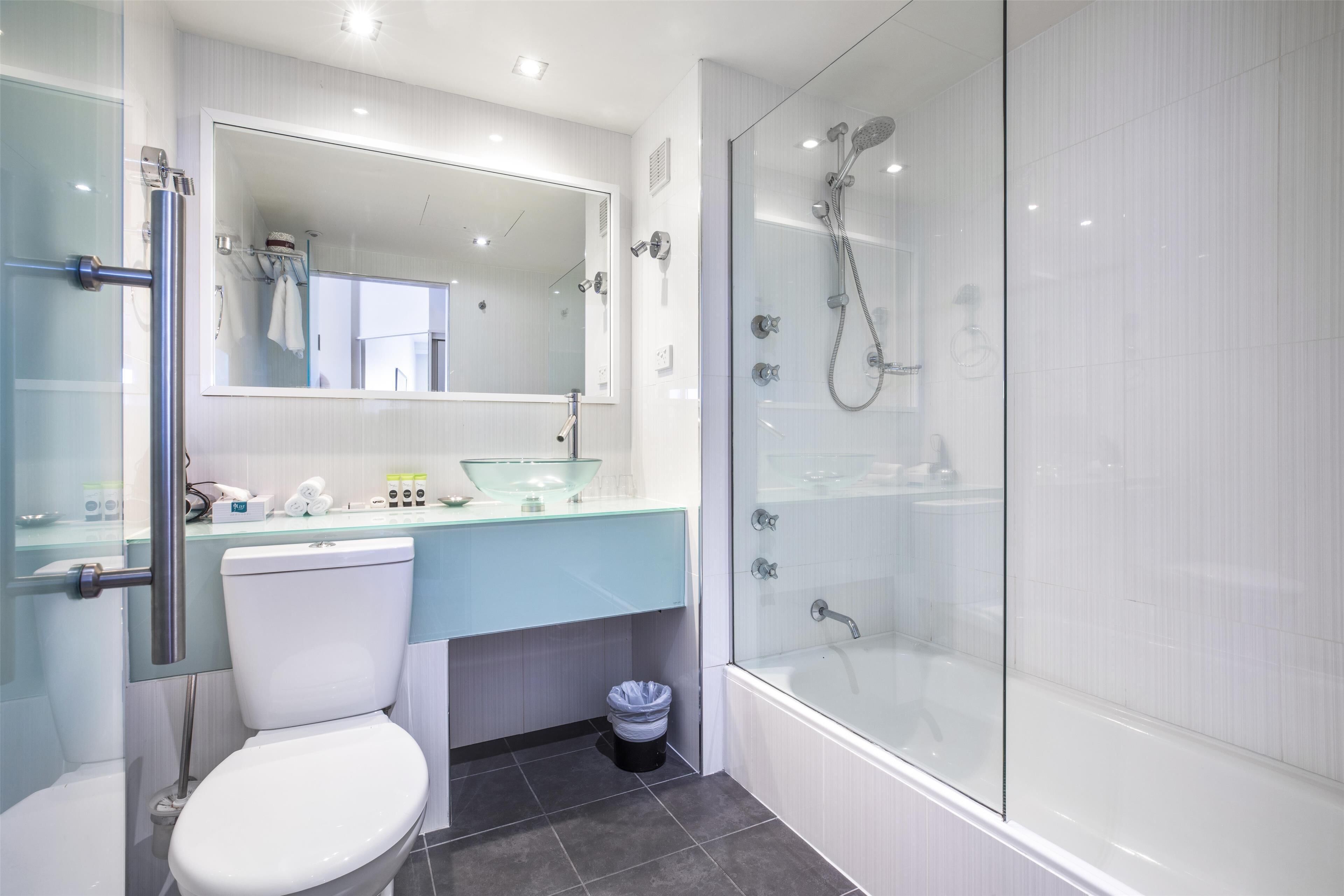 Un baño moderno con ducha envuelta en vidrio, inodoro blanco y lavamanos de vidrio.