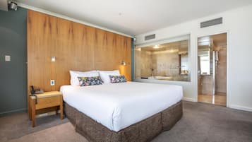 Camera d'albergo con un letto grande, parete rivestita in legno, un comodino con un telefono e un bagno con doccia in vetro.
