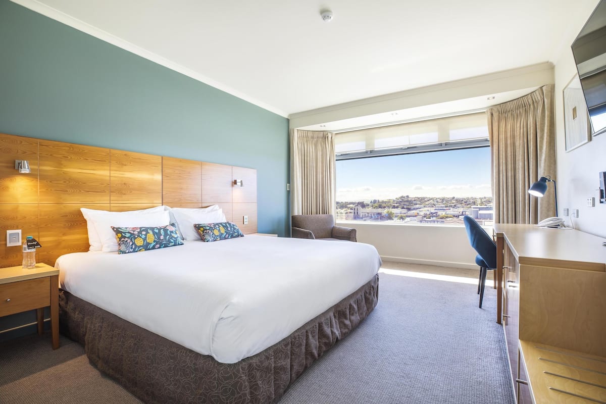 Habitación de hotel con una cama grande, un escritorio, una silla y vistas a la ciudad.