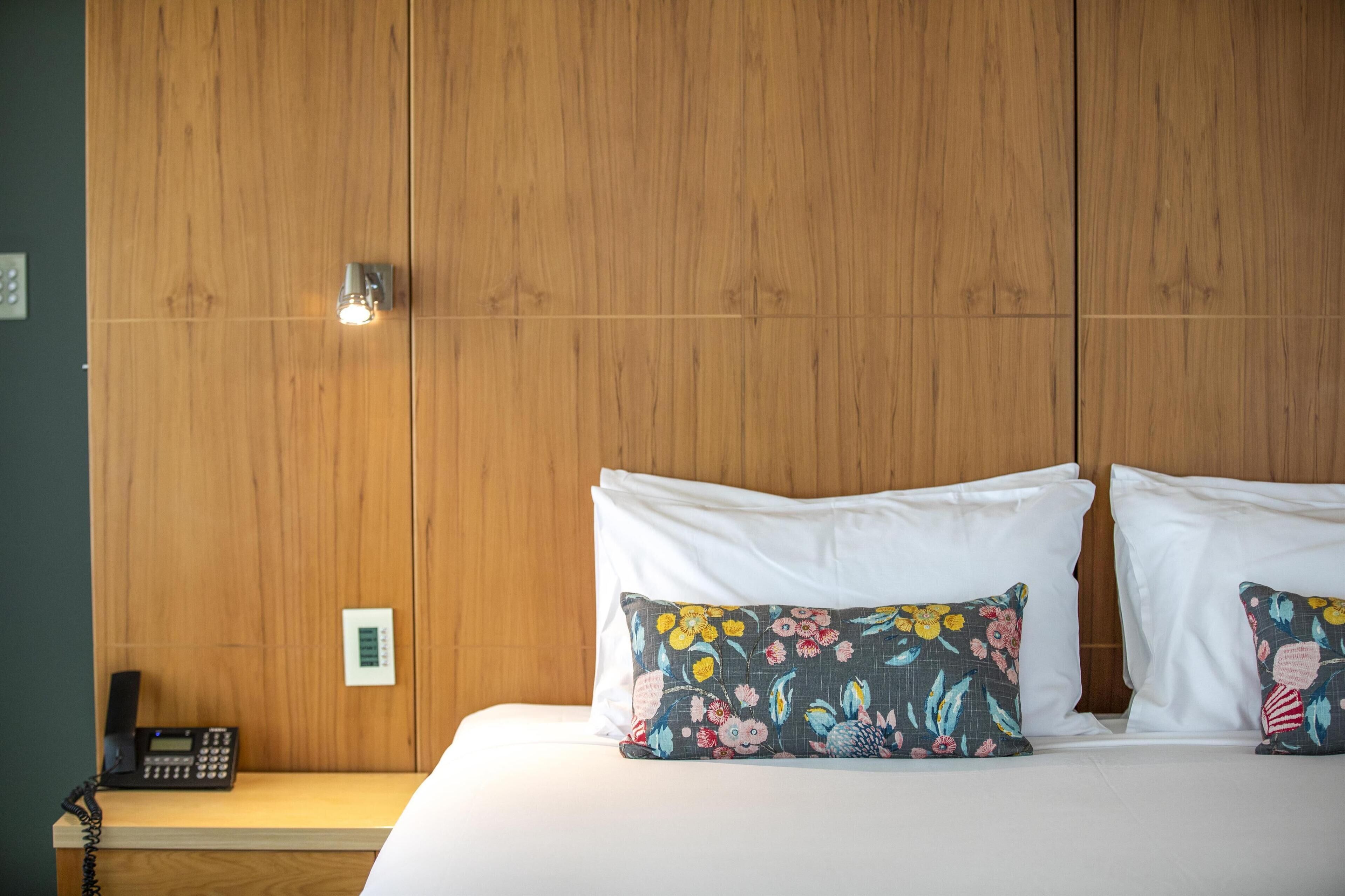 Una habitación de hotel con un cabecero de madera, un teléfono y dos almohadas estampadas con motivos florales.