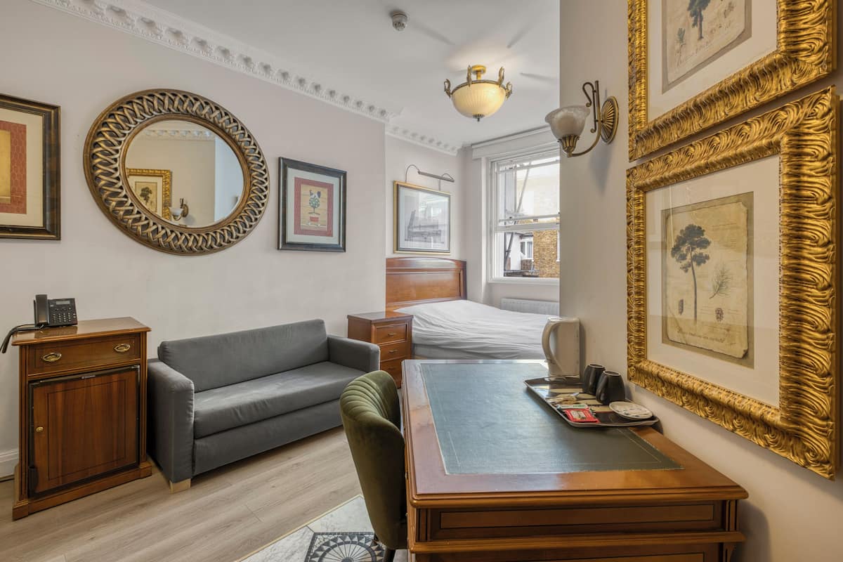 A hotel room with a wooden desk, a grey sofa, a round mirror, and framed pictures on the walls.