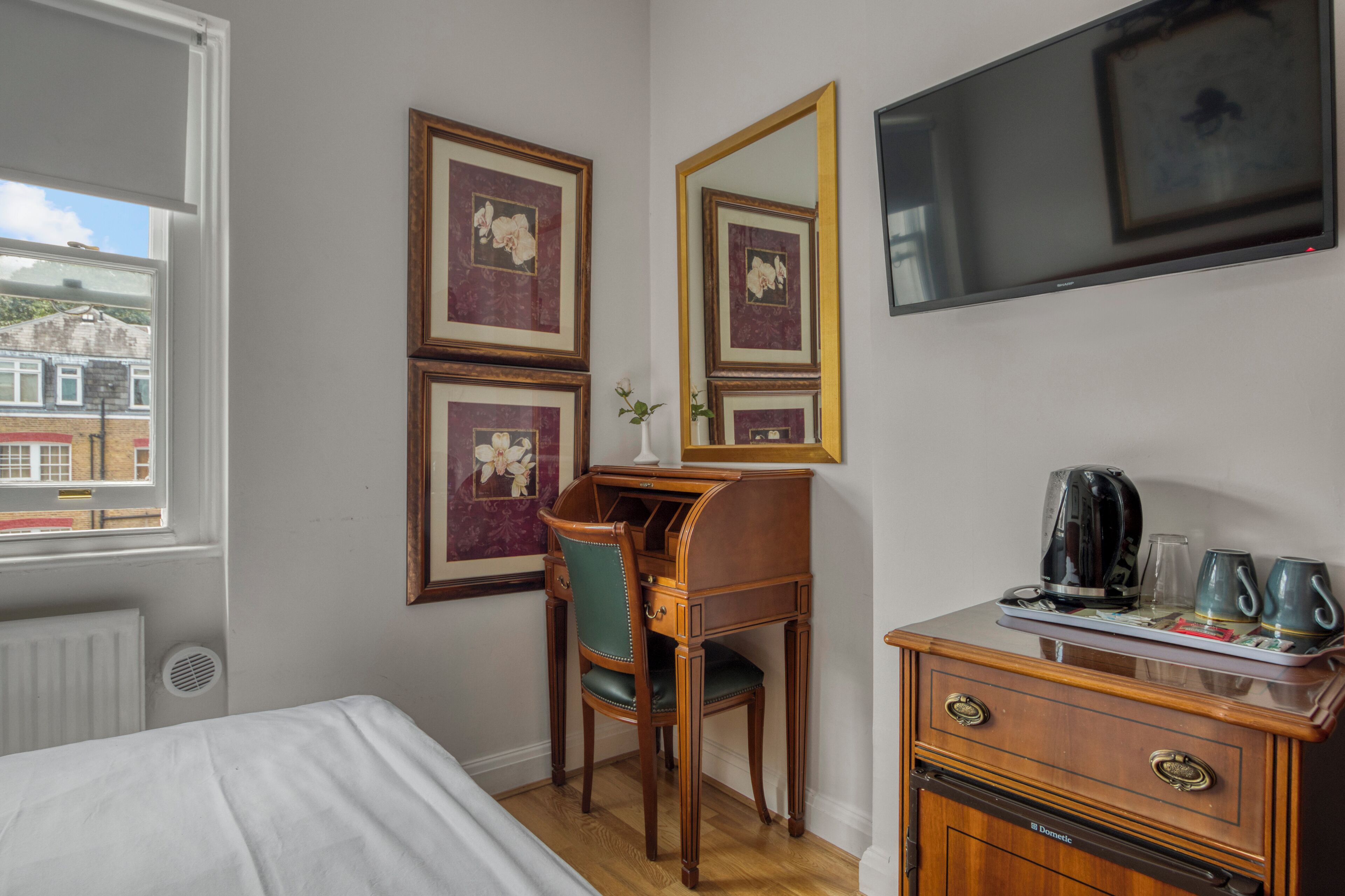 Habitación de hotel con cama, escritorio con silla, cómoda, espejo y televisión en la pared.