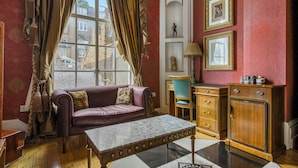 A room with a purple sofa, a marble table, wooden cabinets, and a view through a window with curtains. - Opulence Boutique Hotel (London)