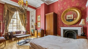 A room with a bed, a sofa, a wooden cabinet, a fireplace, and a large mirror on the wall. - Opulence Boutique Hotel (London)