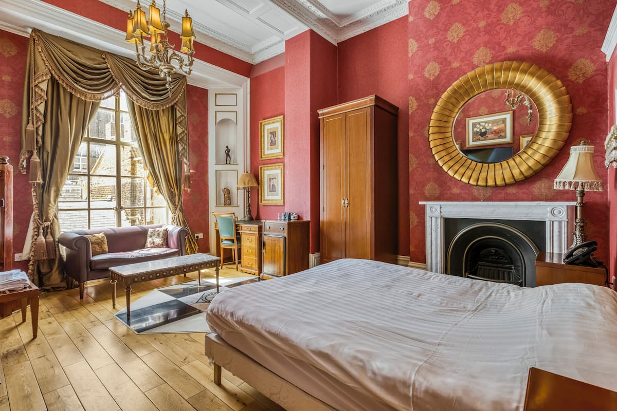 A room with a bed, a sofa, a wooden cabinet, a fireplace, and a large mirror on the wall.