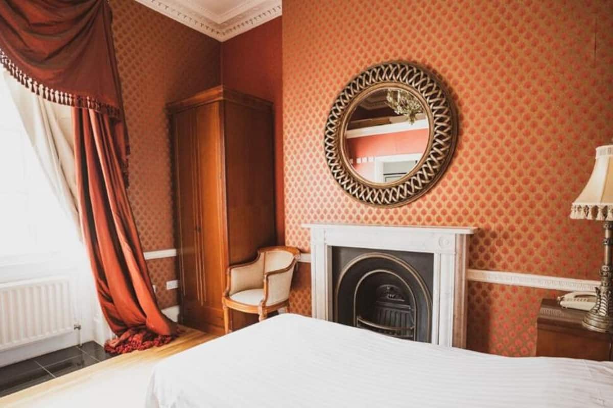 A hotel room with a bed, a fireplace, a mirror, a chair, and a lamp.