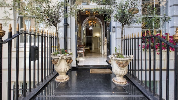 A grand entrance with a black iron gate, two large urns with plants, and a staircase leading to the interior. - Opulence Boutique Hotel (London)