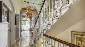 A grand staircase with ornate white railings and a chandelier. - Opulence Boutique Hotel (London)