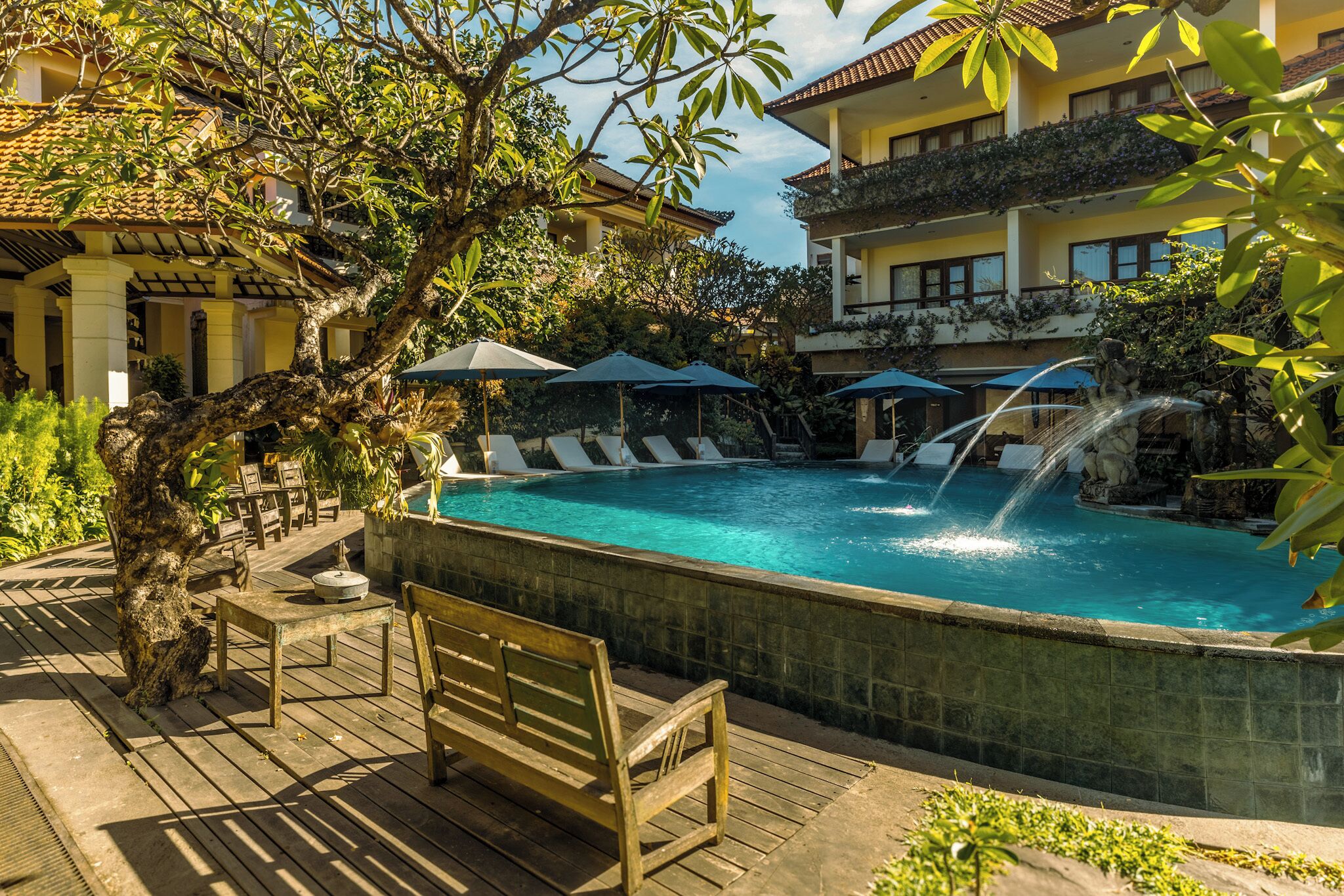 Zona de piscina con sillones de descanso, sombrillas y una cascada.