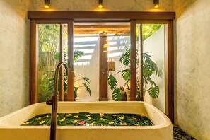 Un baño con bañera, puerta de madera y plantas en macetas.
