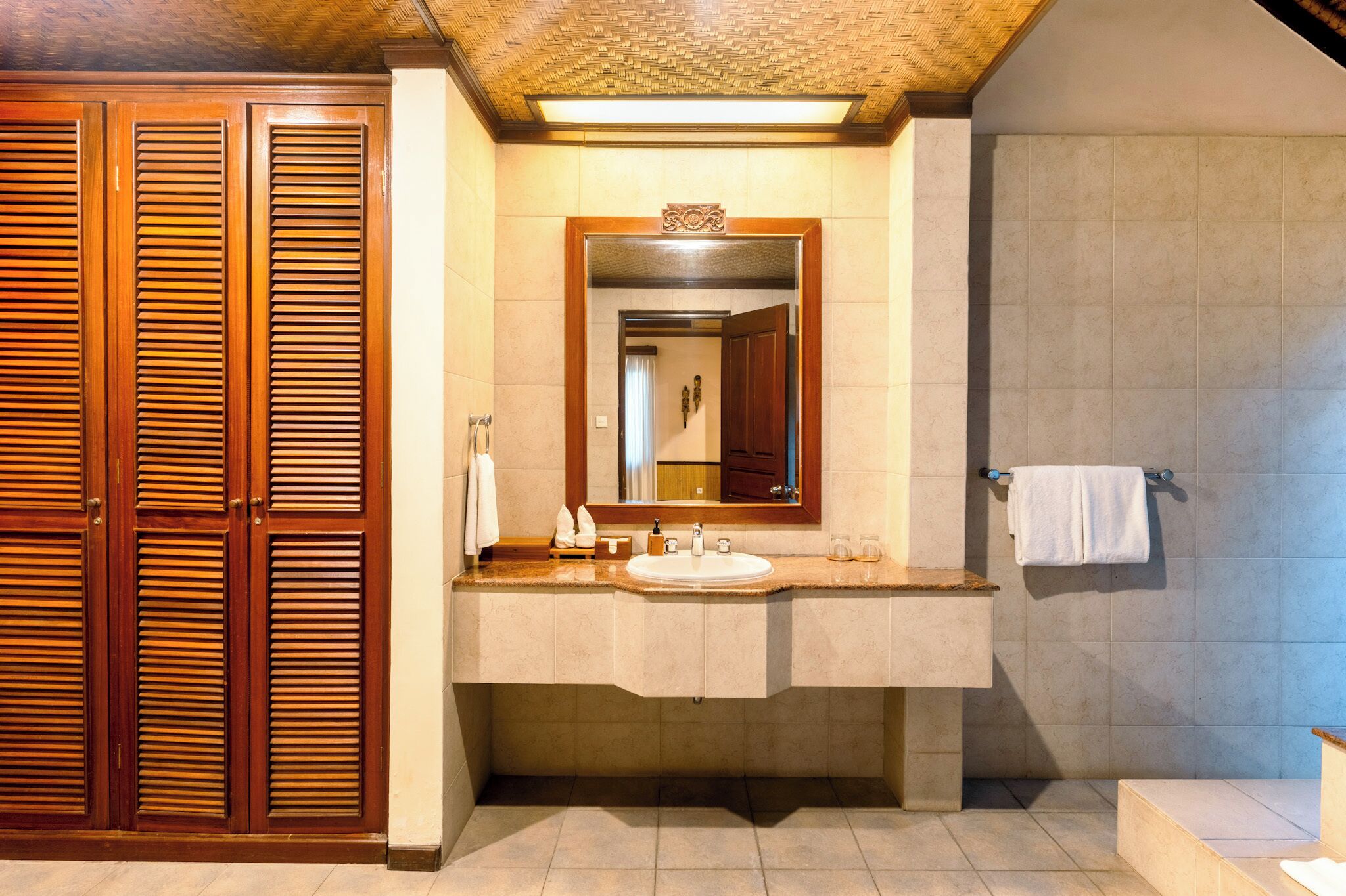 A bathroom with a wooden vanity, a large mirror, and a tiled shower area.