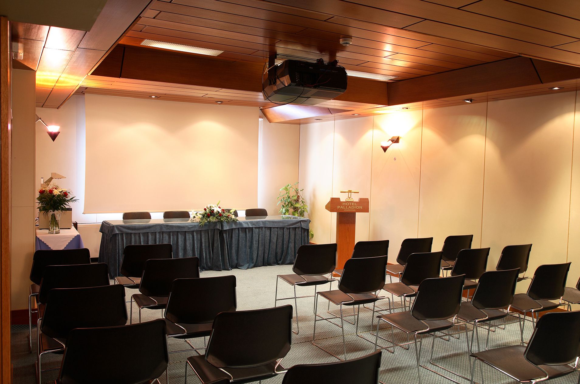 Een vergaderzaal met een lange tafel, stoelen, een projecter en een spreekgestoelte.