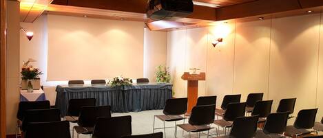 Una sala de conferencias con una larga mesa, sillas, un proyector y un atril.
