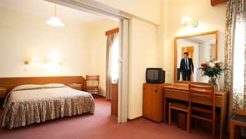 Habitación de hotel con cama, escritorio, silla, televisor, espejo y un florero con flores.