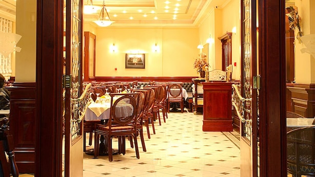 A restaurant with a classic interior, featuring wooden doors, a chandelier, and a long dining table with chairs.
