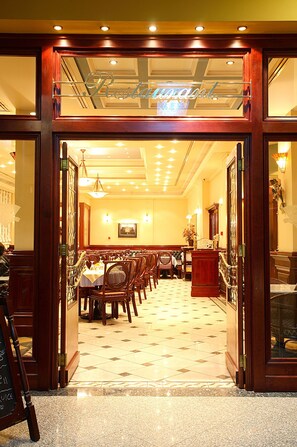Een restaurant met een klassiek interieur, met houten deuren, een kroonluchter en een lange eettafel met stoelen.