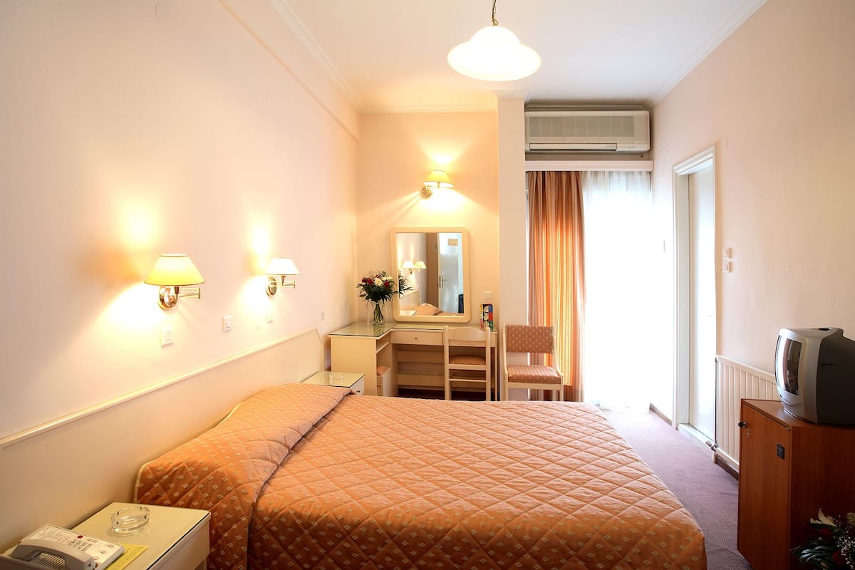 Een hotelkamer met een bed, nachtkastje, lamp, spiegel, dressoir en een airconditioning.