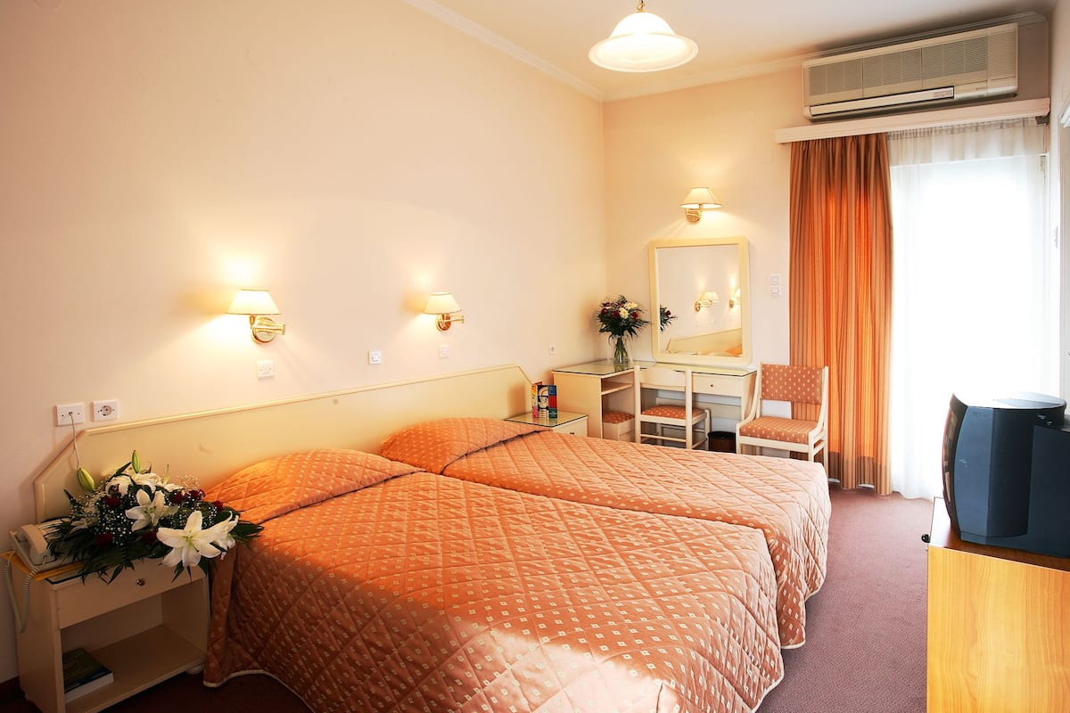 Een hotelkamer met twee bedden, een bureau, een stoel, een spiegel en een airconditioner.