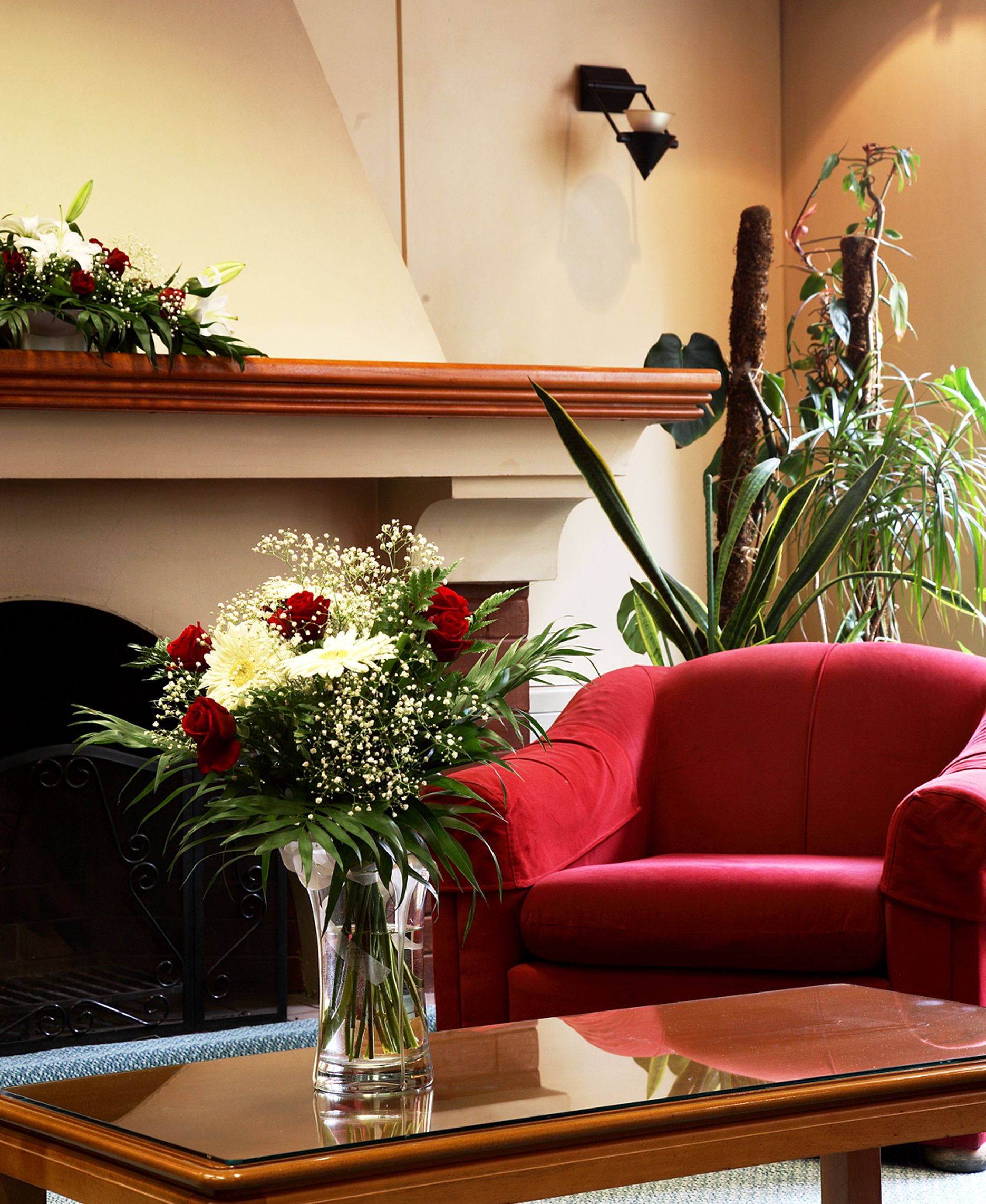 Una habitación con un sillón rojo, una mesa de centro de vidrio y un jarrón con flores.