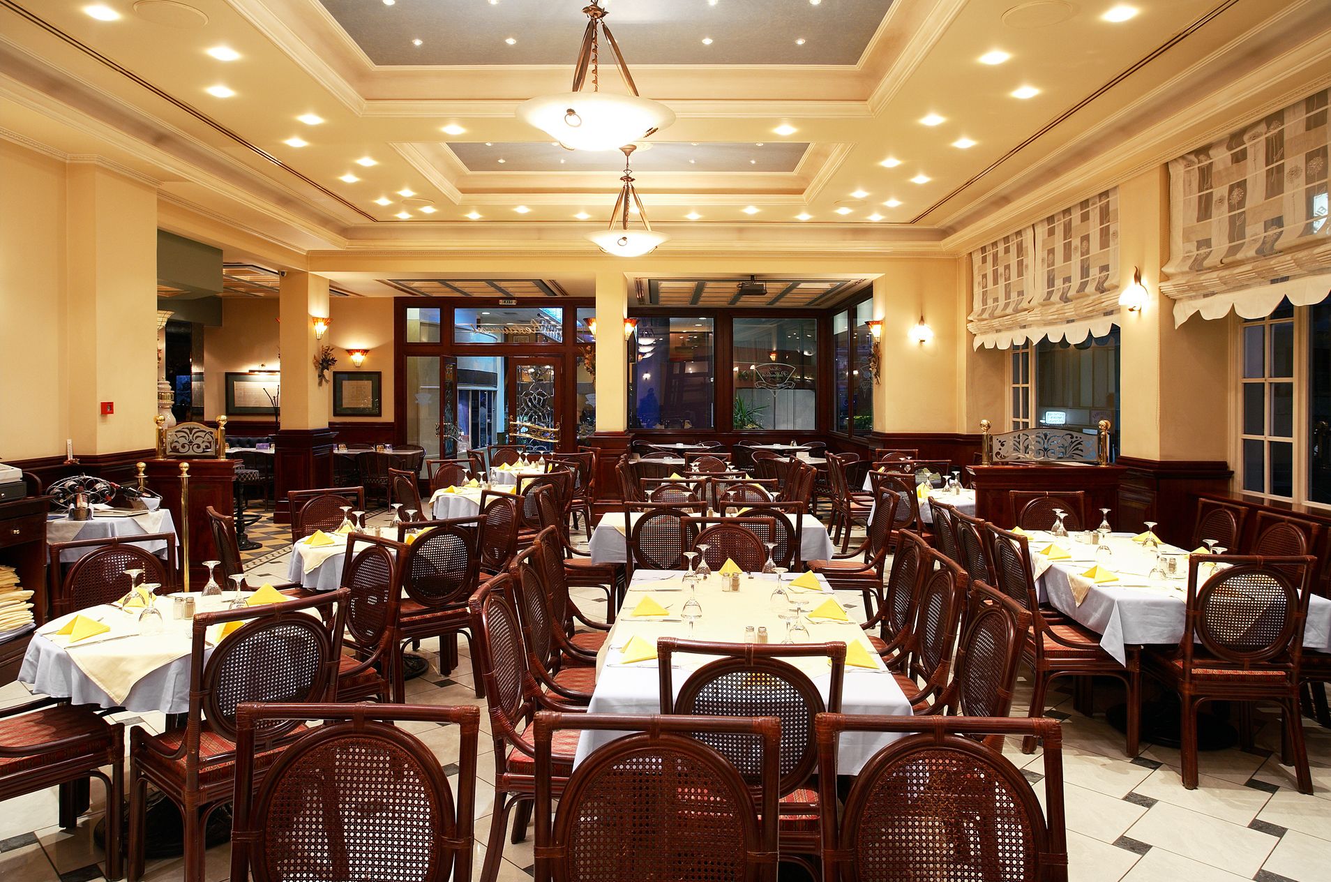 Un restaurante espacioso con múltiples mesas y sillas, un candelabro y ventanas grandes.