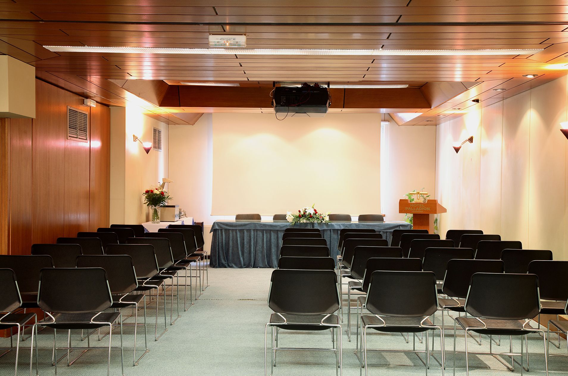 A conference room with rows of chairs, a table with a blue tablecloth, and a podium with the hotel name.