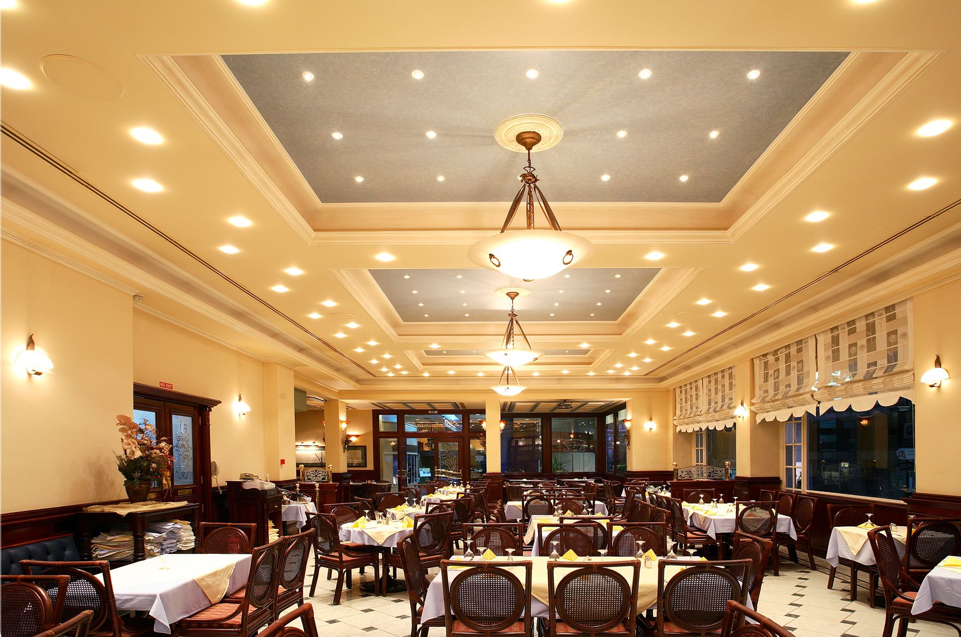Un comedor espacioso con varias mesas y sillas, un candelabro y vistas al exterior a través de amplias ventanas.