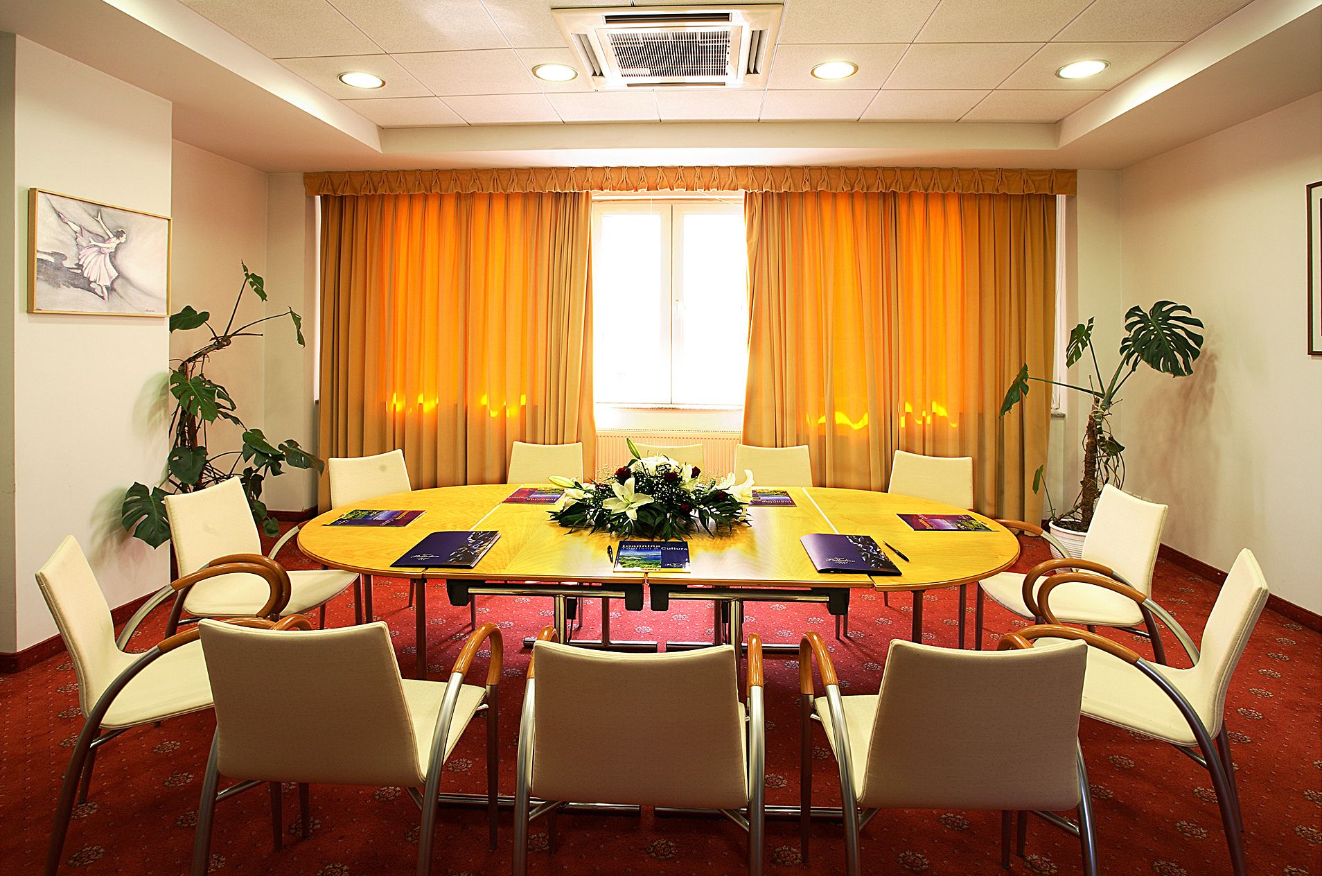 A conference room with a round table, eight chairs, and orange curtains.