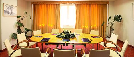 Un salón de conferencias con una mesa redonda, ocho sillas y cortinas naranjas.