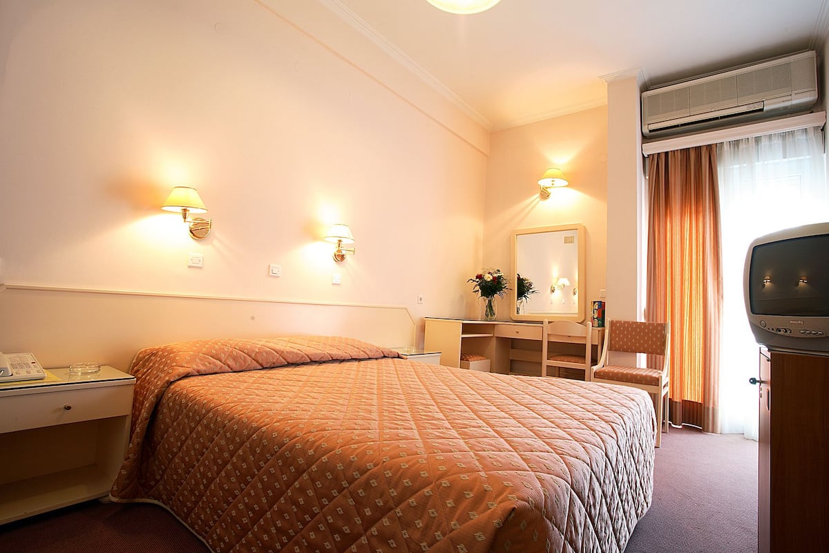 Een hotelkamer met een bed, nachtkastje, lamp, spiegel, dressoir en een televisie.