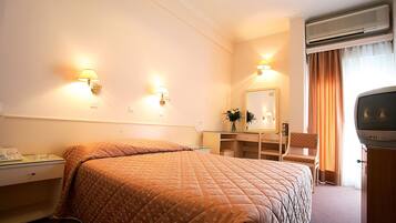 A hotel room with a bed, bedside table, lamp, mirror, dresser, and a television.