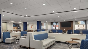 A modern hotel lobby with seating areas, a coffee station, and a large TV screen.
