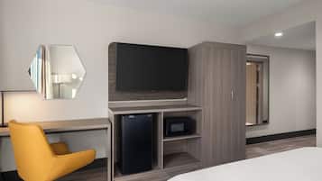 A hotel room with a bed, a desk with a chair, a television, a microwave, and a wardrobe.