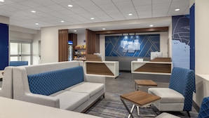 A modern hotel lobby with seating areas, a reception desk, and a wall-mounted screen displaying the hotel name.