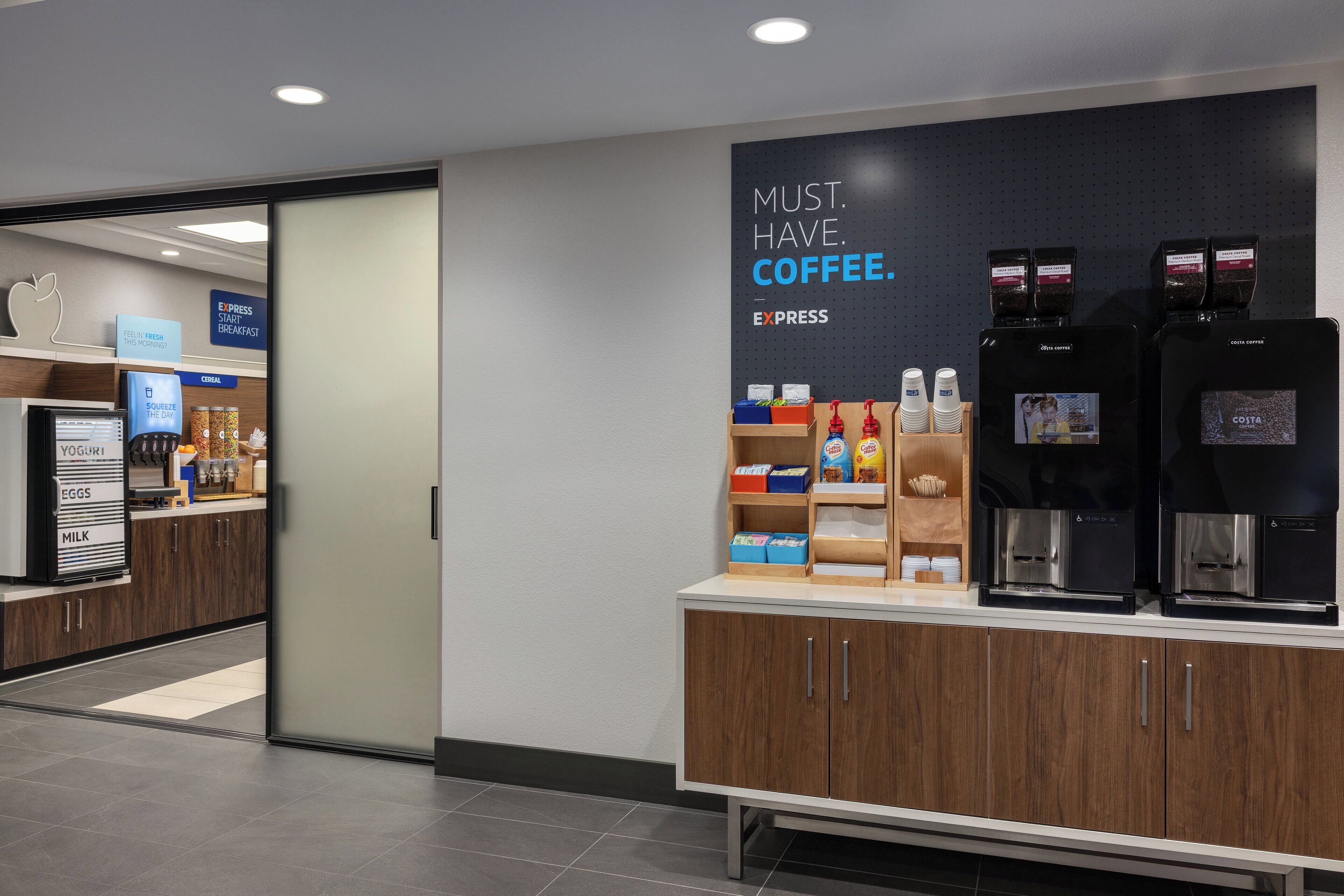 Una estación de café moderna con máquinas de café de la marca y un cartel que dice "NECESARIO. CAFÉ."