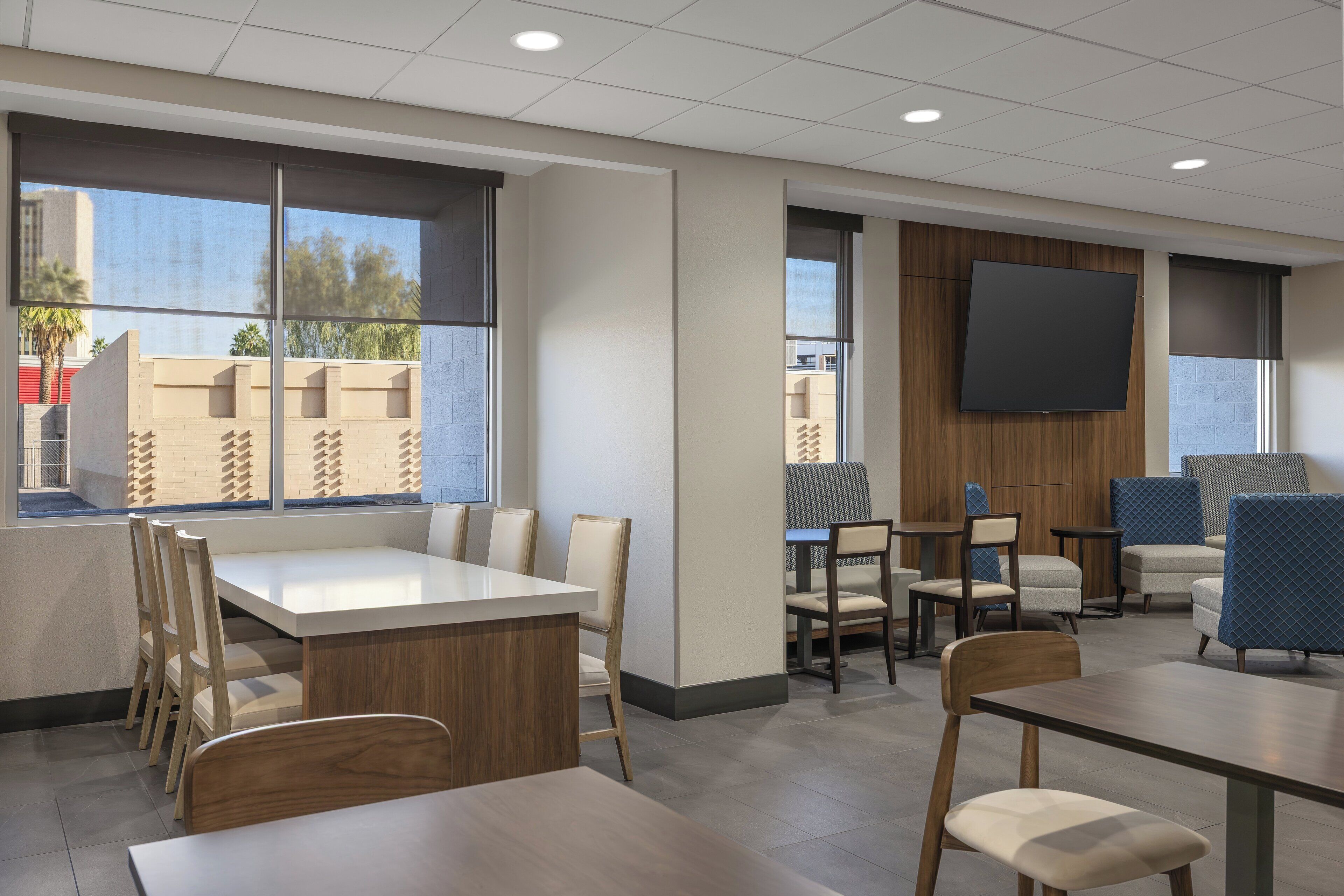 A modern conference room with a large table, several chairs, a flat-screen TV, and large windows offering a view of the cityscape.