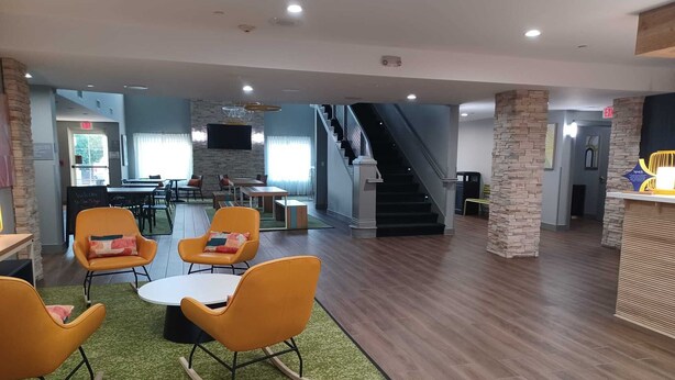 Un vestíbulo amplio con escalera, zona de recepción y área de descanso con sillas anaranjadas y una mesita.