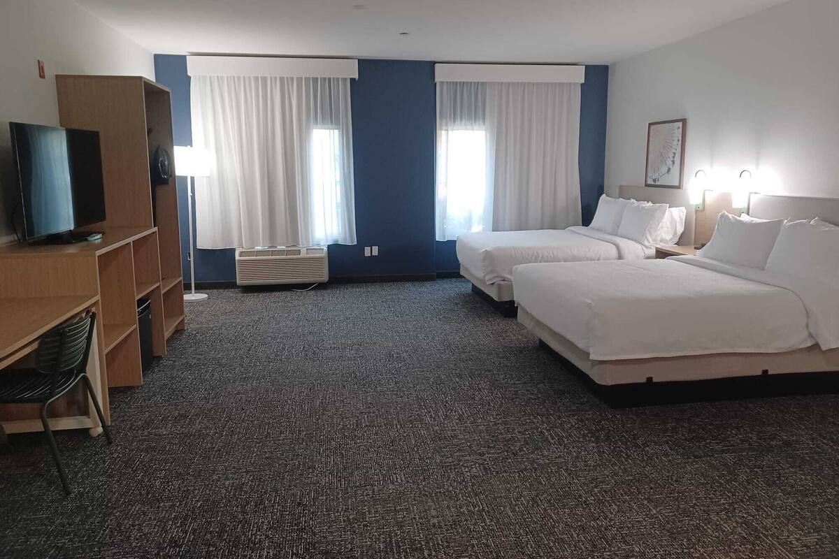 A hotel room with two beds, a TV, a desk, and a chair.