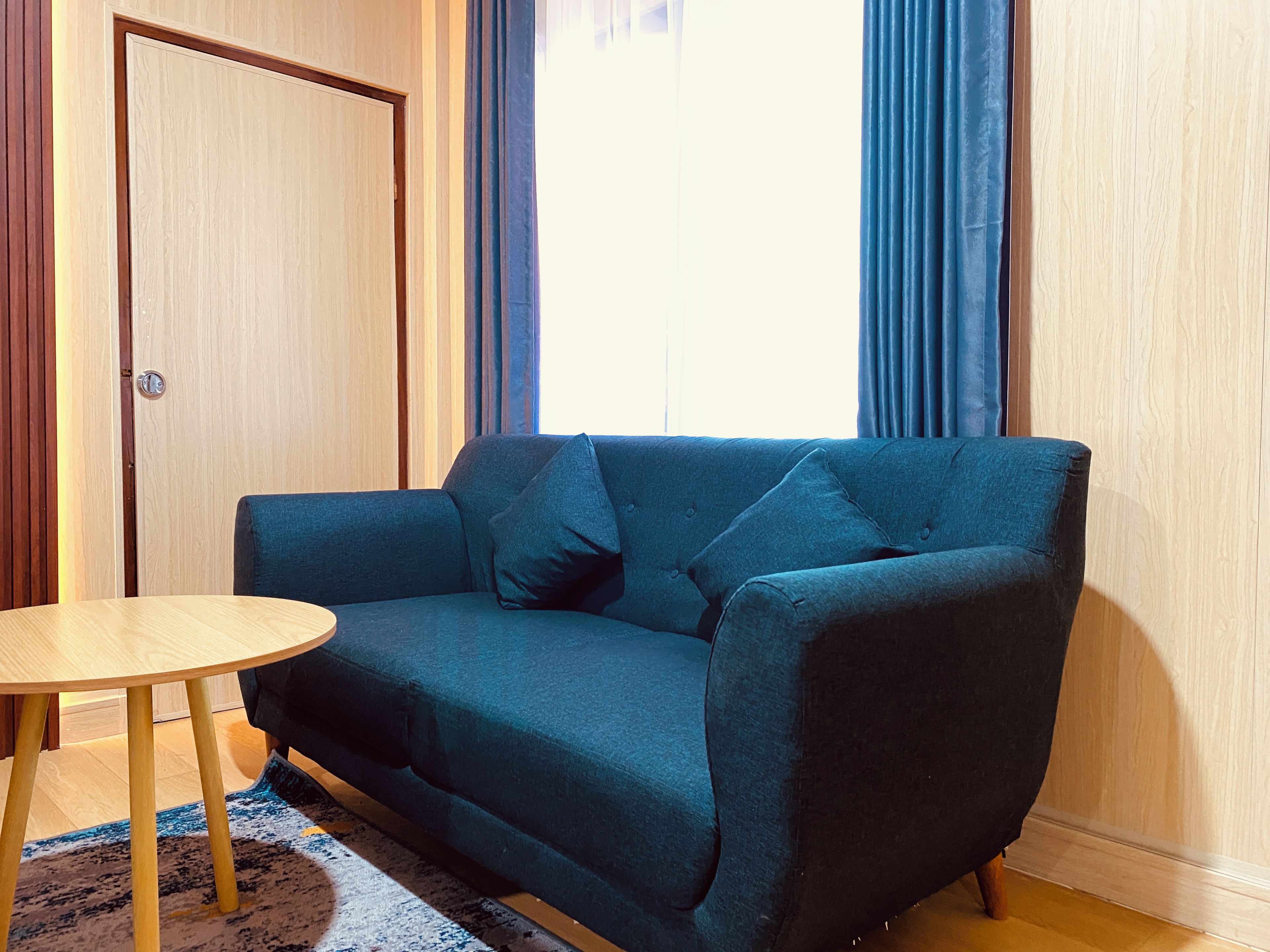 A room with a dark blue sofa, a round wooden table, and a patterned rug.