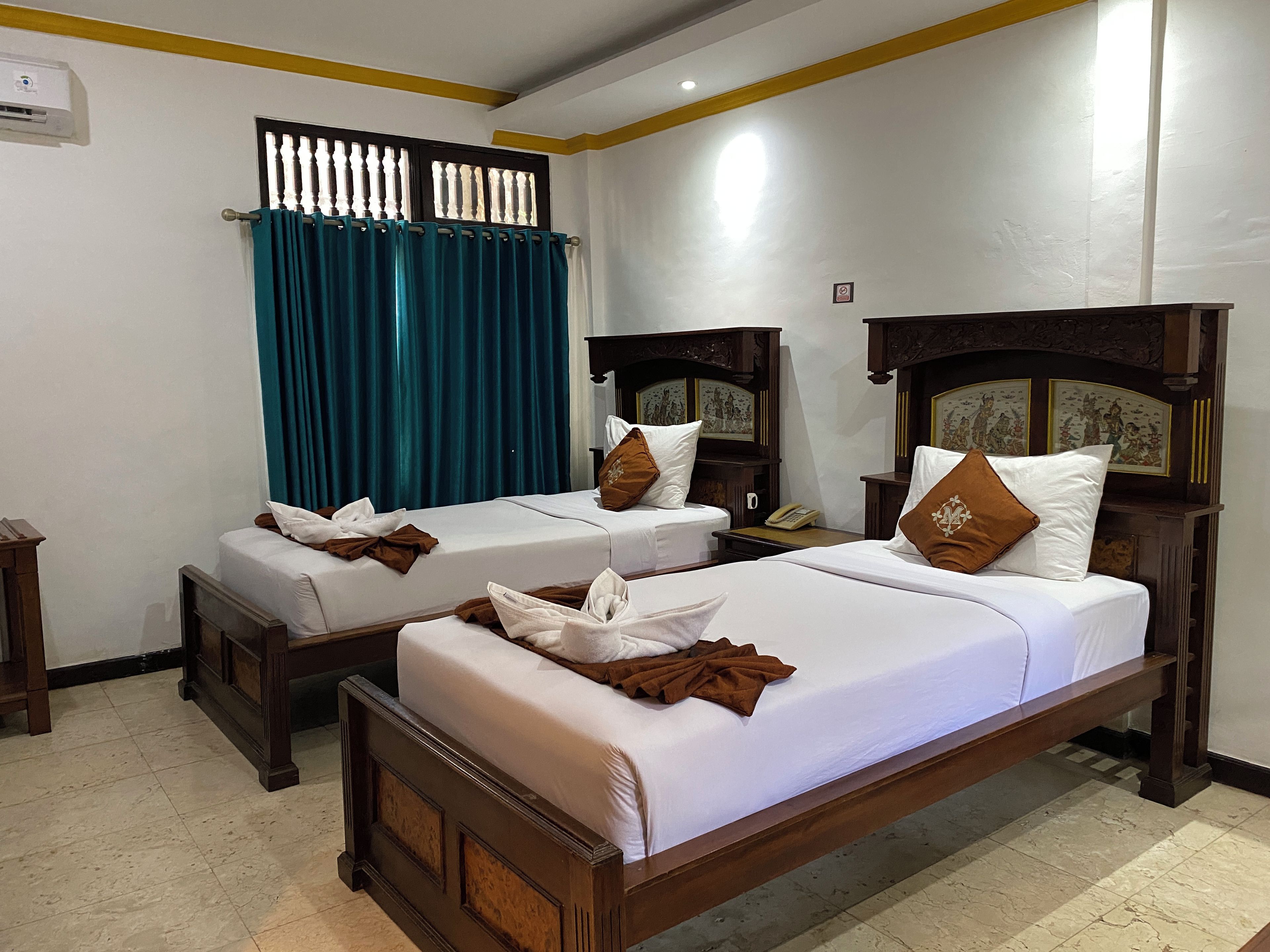A hotel room with two beds, a window with curtains, a wall-mounted air conditioner, and a telephone on the nightstand.
